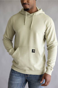 A man wearing a light sage green Carhartt hoodie with a front kangaroo pocket and drawstrings, paired with blue jeans, against a neutral gray studio background.