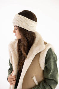 Carhartt Satin Lined Knit Headband in Oat Milk worn with a fleece vest, olive long-sleeve top, and jeans