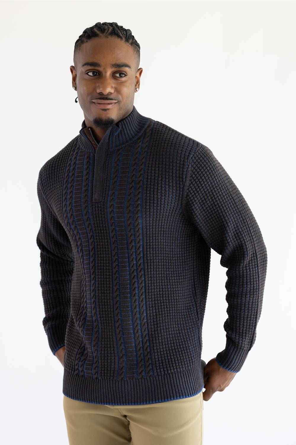 A man wearing a dark brown blue quarter-zip knit sweater with textured vertical cable patterns, paired with khaki pants, against a plain white studio background.