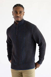 A man wearing a dark brown blue quarter-zip knit sweater with textured vertical cable patterns, paired with khaki pants, against a plain white studio background.