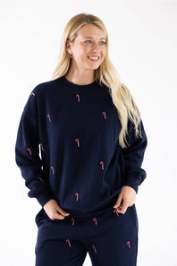 A woman wearing a navy blue crewneck fleece sweatshirt with an all-over pink and white candy cane embroidery pattern, paired with matching navy sweatpants.
