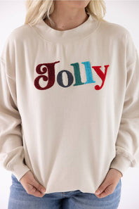 Detail shot of a woman wearing a beige fleece mock-neck sweatshirt featuring multicolored chenille patch lettering that reads "Jolly" across the chest.