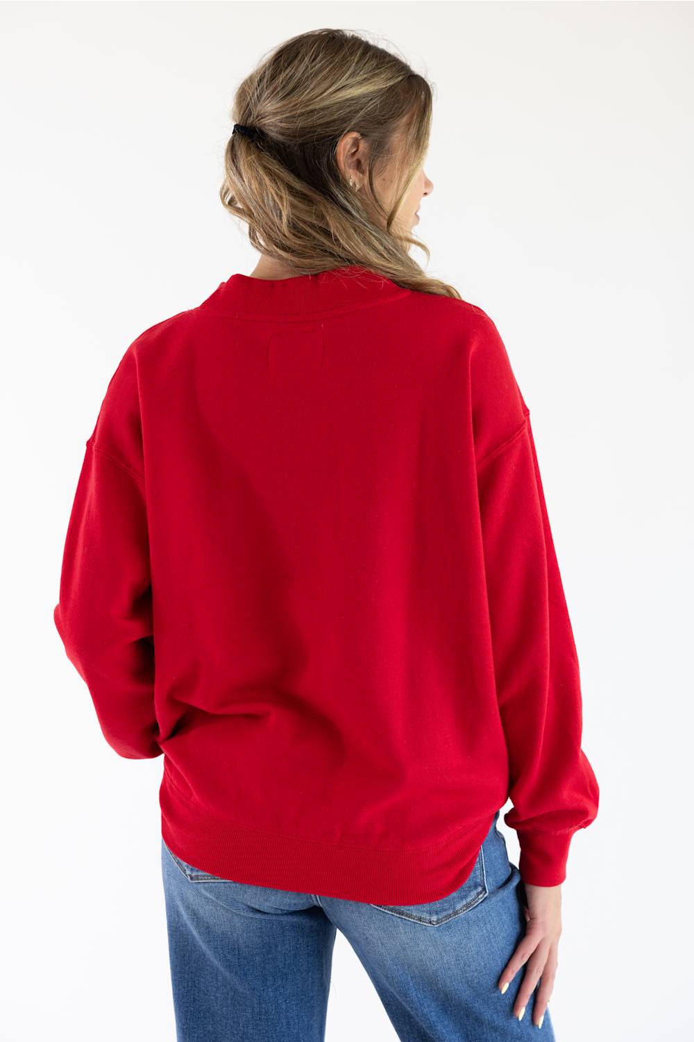 Back view of a woman with her hair pulled back, wearing the red 1897 Active USA mock neck sweatshirt and blue jeans against a plain white studio background.