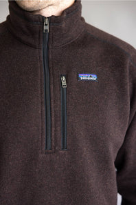 Close-up of a person wearing a dark brown Patagonia quarter-zip fleece pullover, showing the chest zipper, collar, and the Patagonia logo patch on the left chest.