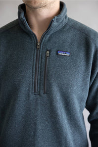 A close-up of a man wearing a Patagonia quarter-zip fleece pullover in a heathered slate blue-gray color. The Patagonia logo is visible on the left chest.