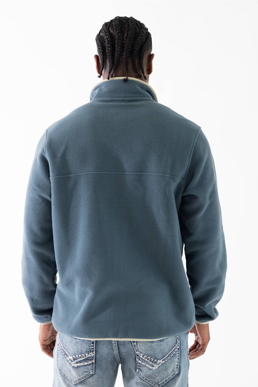 A man viewed from behind wearing a slate blue fleece pullover jacket with a light beige collar, paired with light-wash blue jeans, against a plain white background.