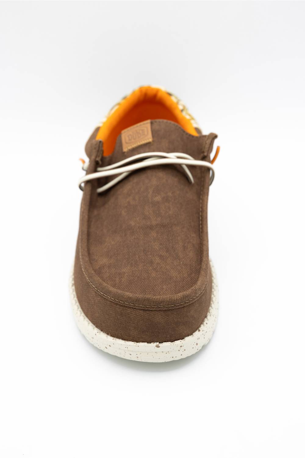 A single brown suede slip-on shoe with white laces, a bright orange interior lining, and a textured off-white sole, shown from a front-facing perspective on a white background.