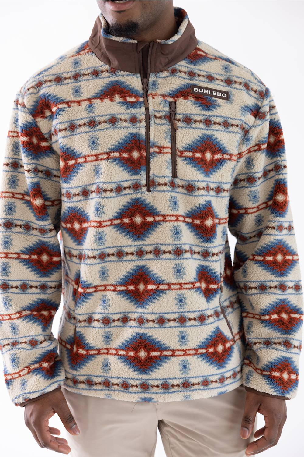 A man wearing a  quarter-zip fleece pullover with a Southwestern geometric pattern in cream, brown, blue, and red, paired with beige pants.
