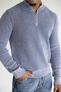 A man wearing a light blue and white vertically striped ribbed quarter-zip sweater with blue jeans, shown from the chest down against a plain white background.