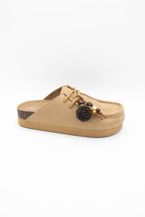 A single tan suede clog-style mule sandal with a thick tan sole, decorative laces, and a dark brown pom-pom ornament on the side, shown against a plain white background.