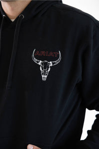 A close-up of a person wearing a black hoodie with a white bull skull graphic and the word 'ARIAT' in red outlined text on the chest.