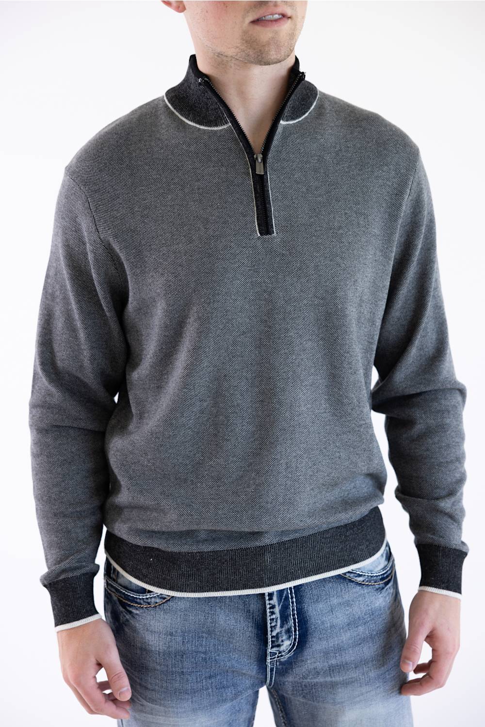 A smiling male model wearing the F/X Fusion Birdseye Knit Quarter Zip in nickel gray, featuring a mock neck, quarter-zip placket, and dark contrasting trim along the collar, cuffs, and hem, paired with classic denim jeans.