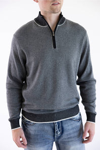 A smiling male model wearing the F/X Fusion Birdseye Knit Quarter Zip in nickel gray, featuring a mock neck, quarter-zip placket, and dark contrasting trim along the collar, cuffs, and hem, paired with classic denim jeans.
