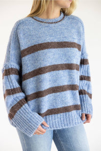 A person wearing a fuzzy knit sweater with horizontal brown stripes on a light blue base, paired with light blue jeans against a plain light background.