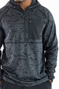 A man wearing a dark gray and black camouflage patterned quarter-zip pullover hoodie with a zippered chest pocket.