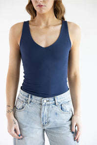 A woman wearing a navy blue tank top and light-wash blue jeans, cropped from the nose down against a plain white background.