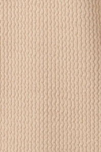 A close-up of a ribbed knit fabric in a warm beige or cream color, showing the vertical wavy texture of the yarn.