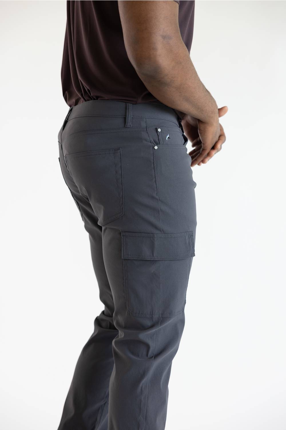 A side profile view of a person wearing dark gray cargo pants and a dark brown t-shirt against a plain white background.