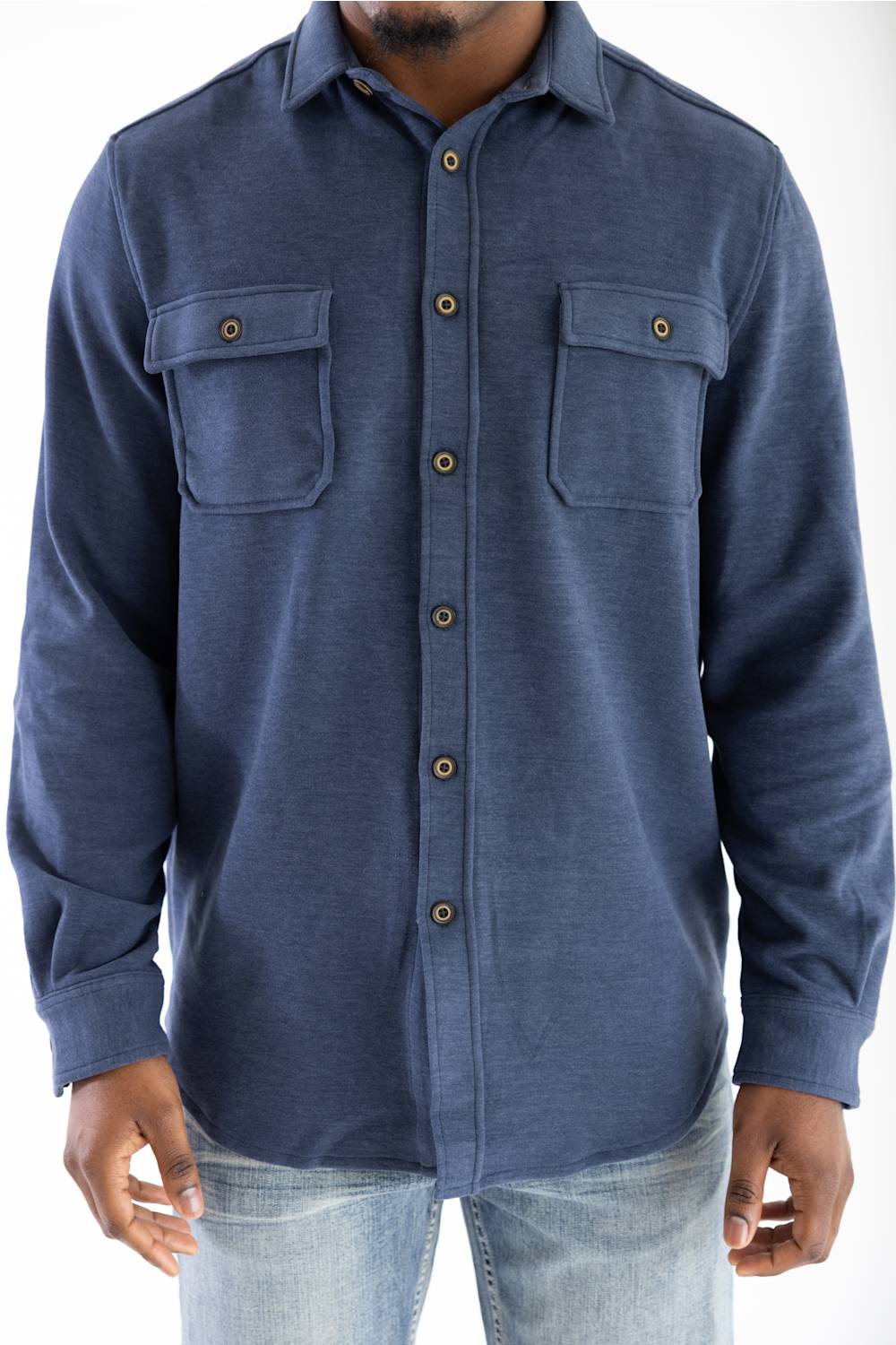 A man wearing a navy blue long-sleeve button-up shirt with two chest pockets and brown buttons, paired with light blue jeans, against a plain white background.