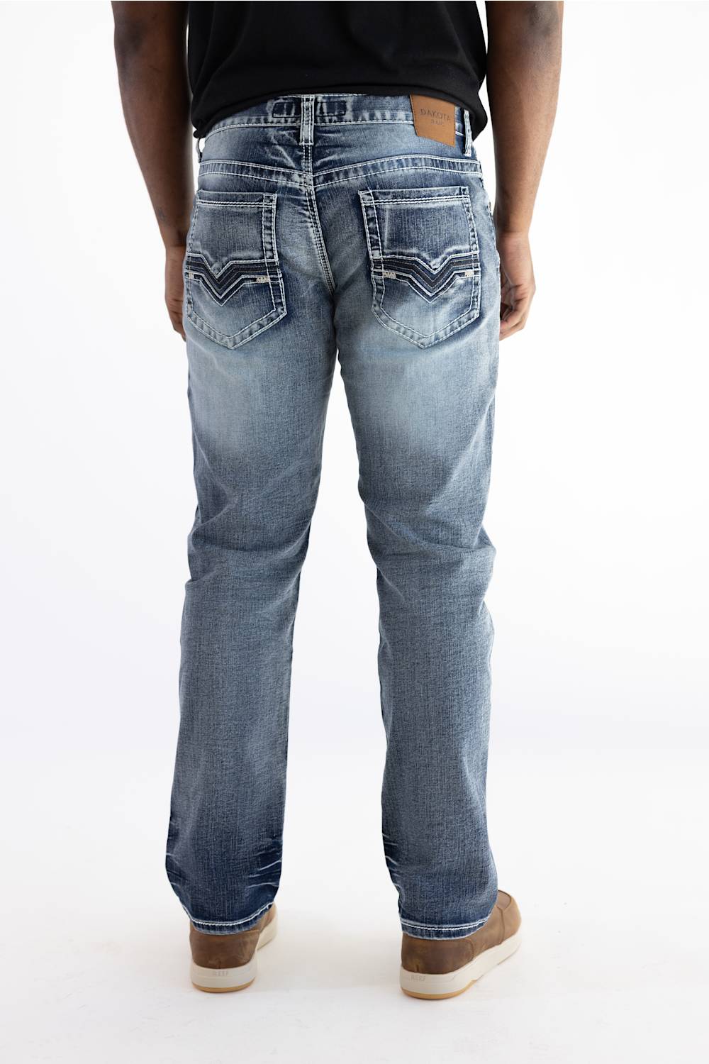 Rear view of a person wearing light blue denim jeans with decorative stitching on the back pockets, a black top, and brown shoes against a plain white background.