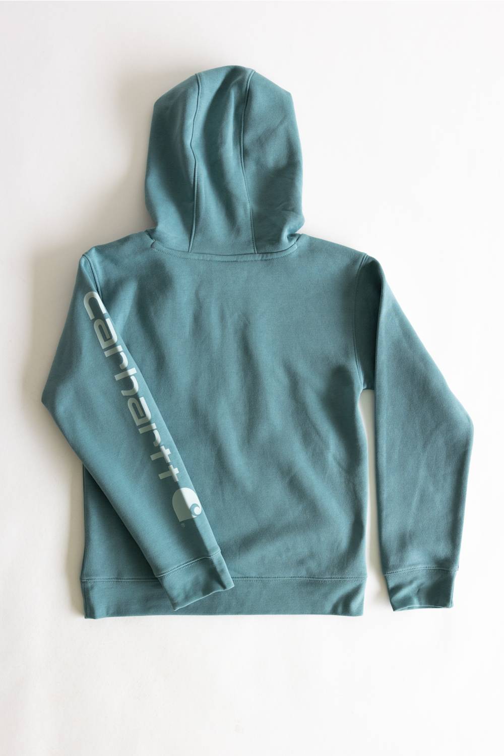A dusty teal blue-green hoodie shown from the back, featuring a vertical white graphic text print down the left sleeve, laid flat on a light off-white background.