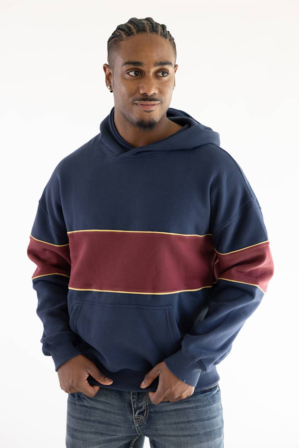 A man wearing a navy blue hoodie with a wide burgundy horizontal stripe across the chest and thin gold trim, paired with blue jeans, against a plain white background.
