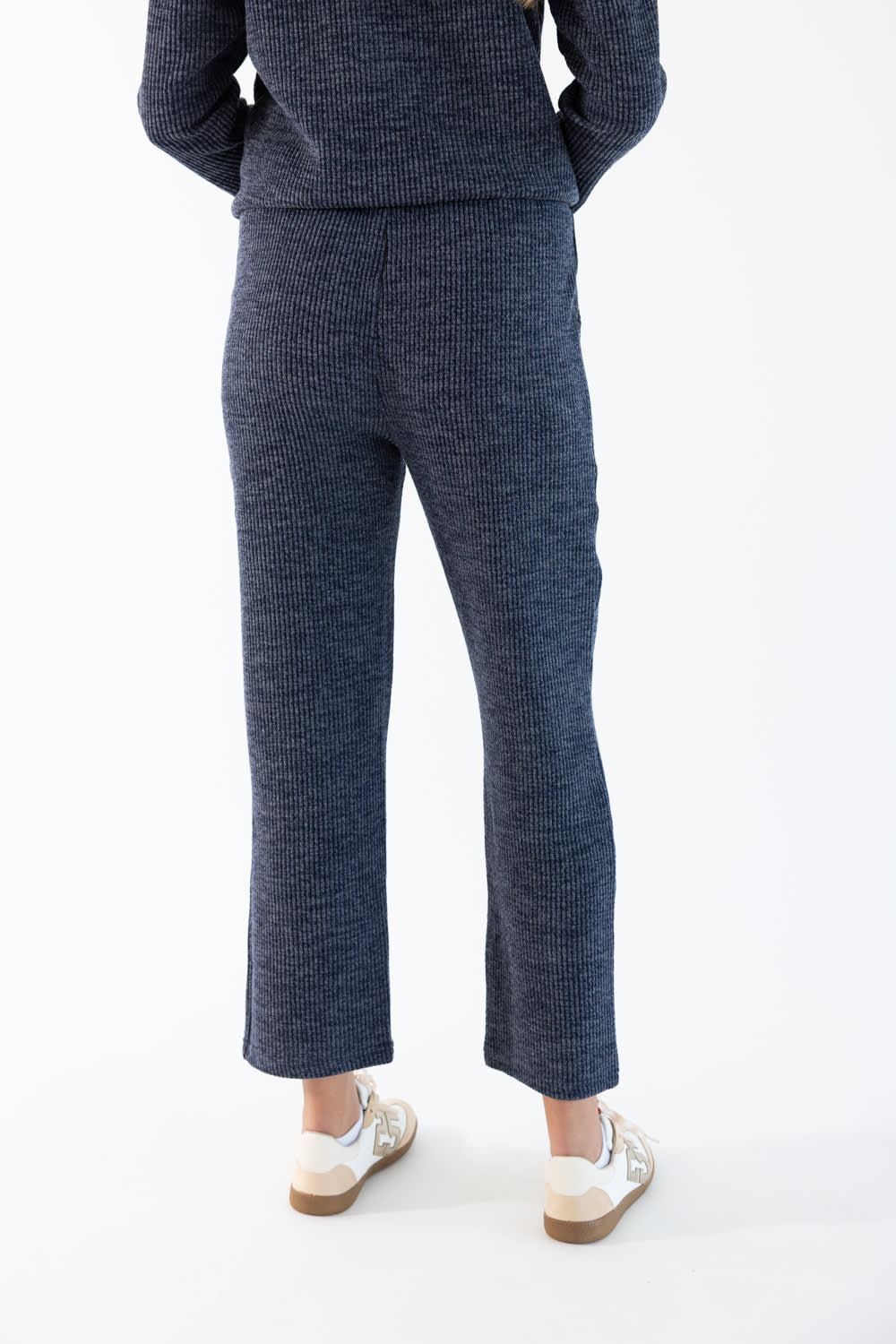 A person shown from the back wearing a matching navy corduroy hoodie and lounge pants, paired with white sneakers, against a plain white studio background.