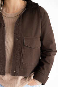 A close-up of a person wearing a dark brown utility jacket over a beige ribbed knit sweater, shown against a plain white background.