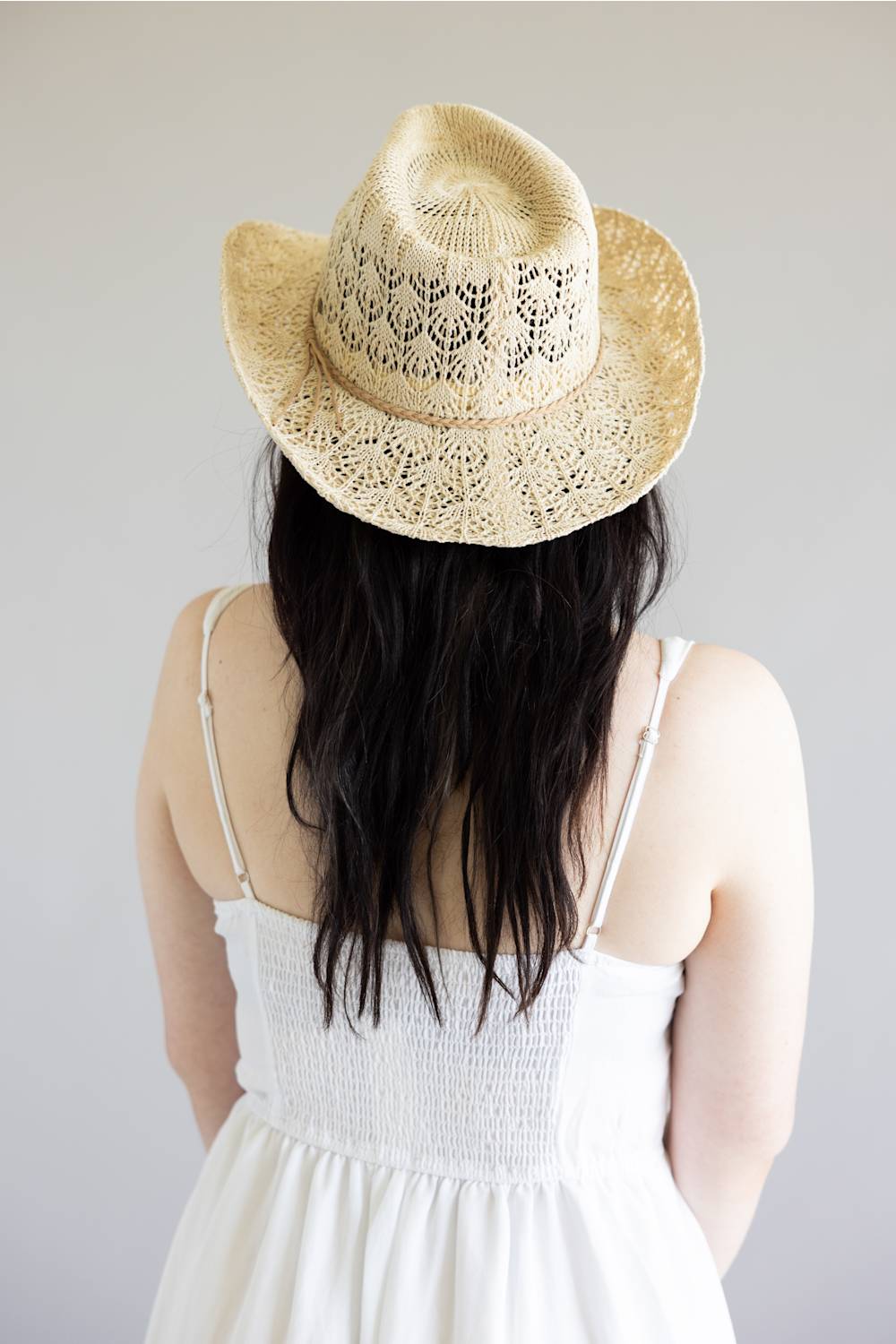 Person wearing a straw hat and white dress against a plain background