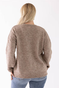 A woman viewed from the back wearing a taupe knit sweater and blue jeans against a plain white background.