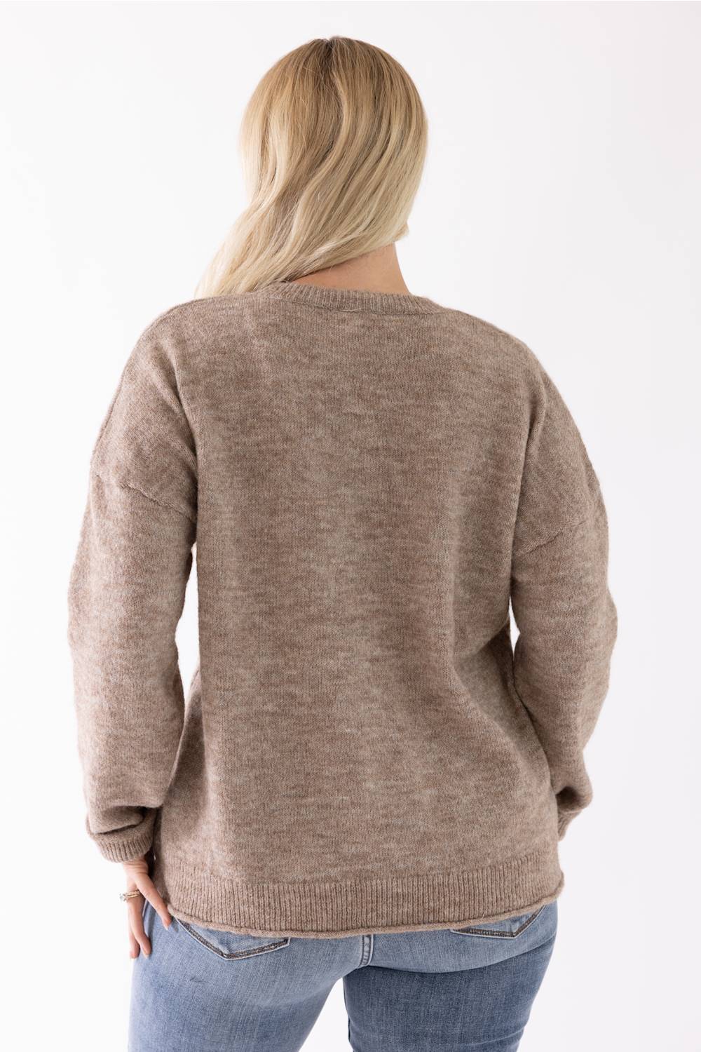A woman viewed from the back wearing a taupe knit sweater and blue jeans against a plain white background.