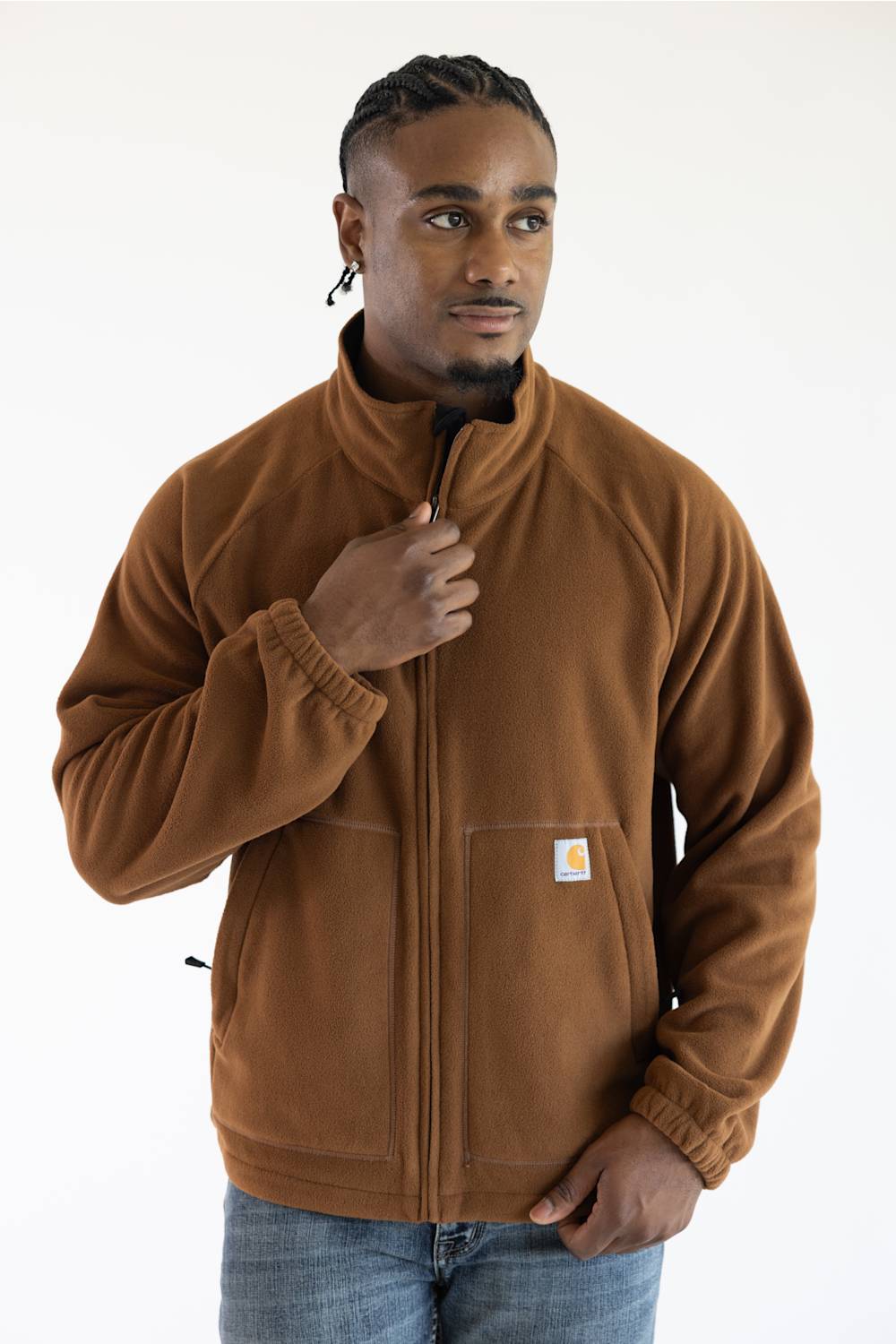 Male model wearing the brown Carhartt Elkhart fleece jacket featuring a full zipper, mock neck collar, elastic cuffs, and the Carhartt logo patch on the left front pocket.