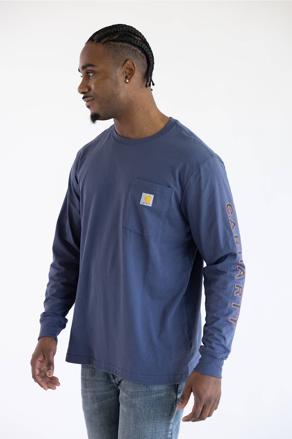 A man wearing a longsleeve Carhartt t-shirt in Superstorm blue with a classic Carhartt patch on the front chest pocket located on the upper left with a Carhartt logo down the left sleeve.
