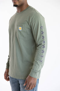 A man wearing the Carhartt Irvine Relaxed Pointer Dog Long Sleeve T-Shirt for Men in Dusty Olive Green featuring a Carhartt logo down the left arm and a classic Carhartt patch logo with front pocket located on the upper left chest.