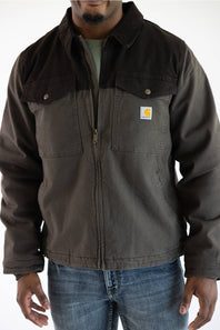 A man in a brown Carhartt jacket and blue jeans stands against a plain white background.