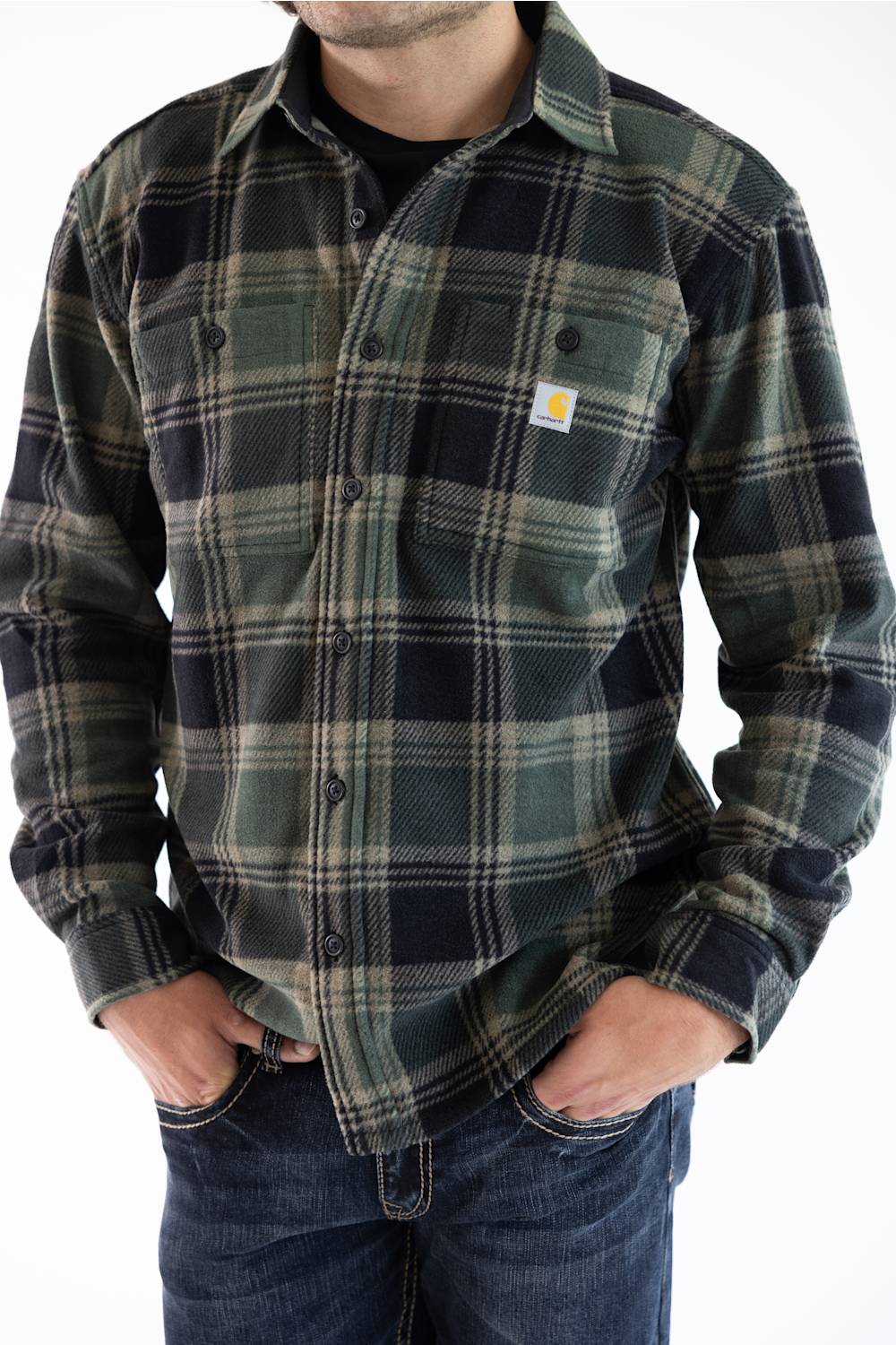 A man wearing a Carhartt long-sleeve flannel shirt in a green and black plaid pattern, paired with blue jeans, against a plain white background.