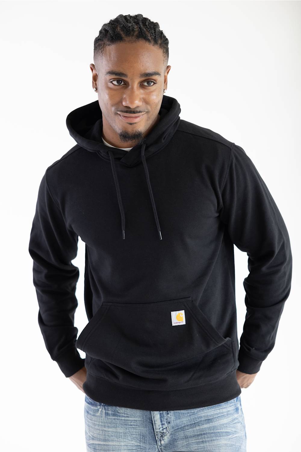 Front view of a man wearing a black Carhartt hooded sweatshirt featuring a front kangaroo pocket with the iconic Carhartt brand logo patch attached.