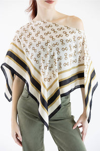A woman wearing a white scarf top with a repeating brown interlocking logo pattern and black and gold striped borders, styled off-the-shoulder over an olive green top.