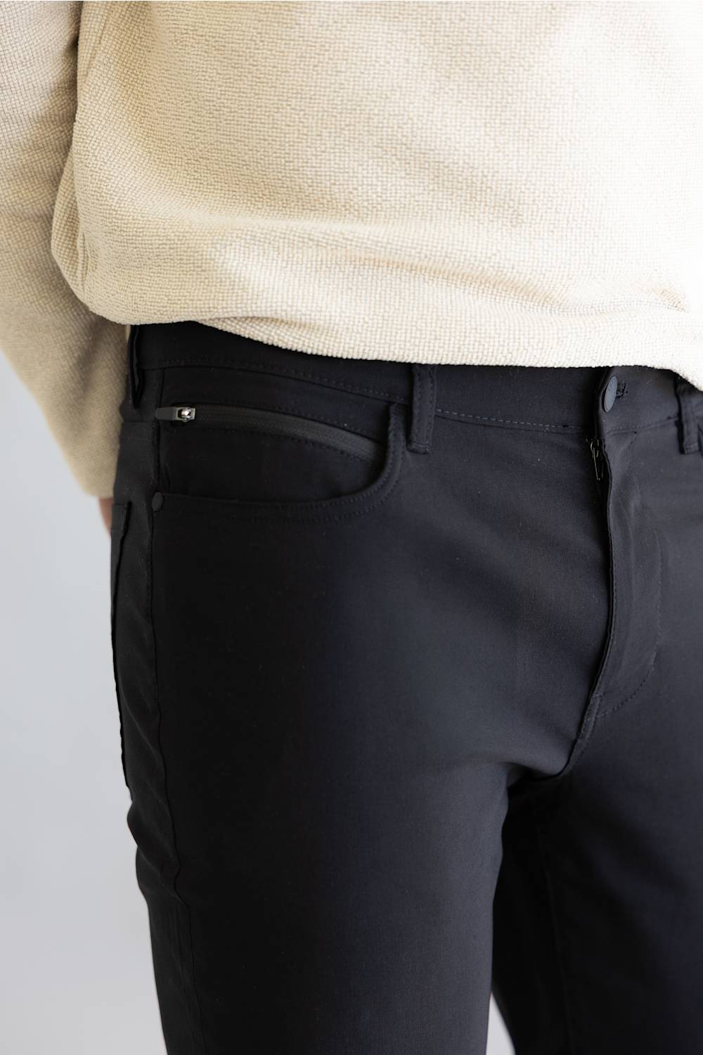 Black pants worn with a beige sweater on a light gray background