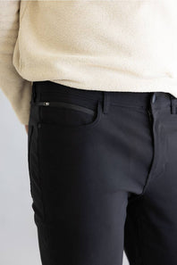 Black pants worn with a beige sweater on a light gray background