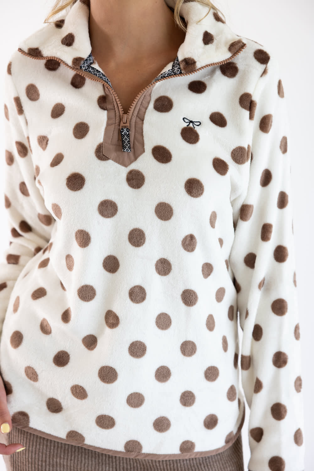 A close-up of a person wearing a cream fleece quarter-zip pullover with brown polka dots and a brown zipper trim.