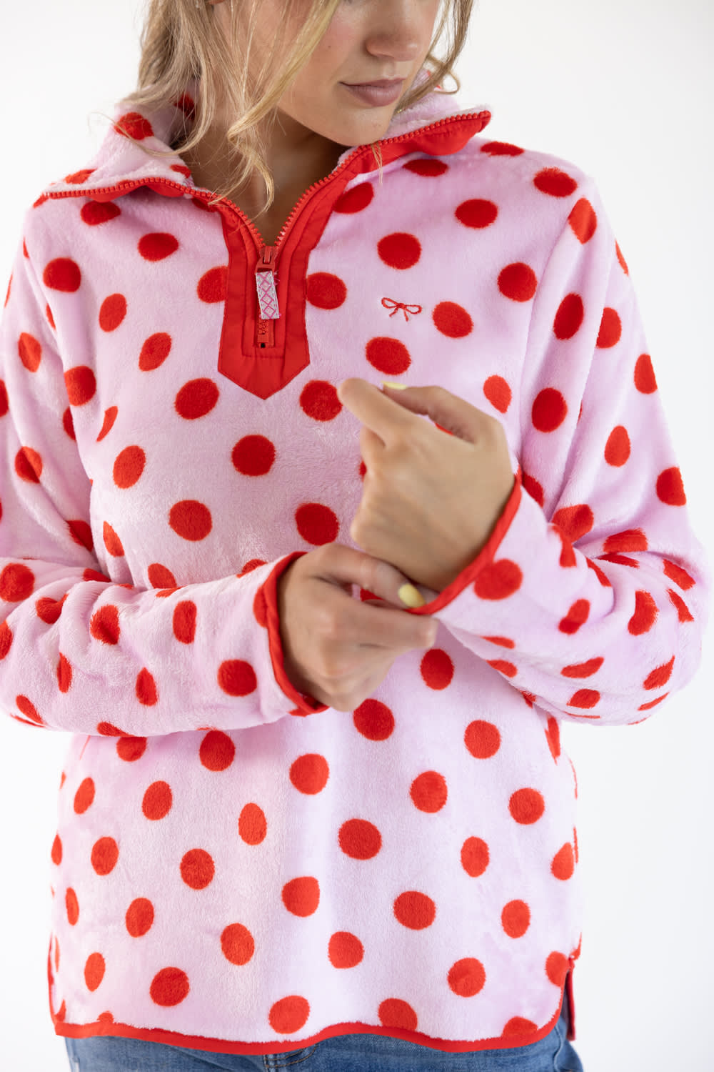 A woman wearing a pink fleece pullover with red polka dots and a red half-zip collar, shown from the chest down against a plain white background.