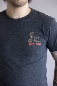 Close-up of a person wearing a dark blue t-shirt with a Burlebo Outdoors logo on a plain background. The shirt is Burlebo Duck Wild Tee for Men in Heather Black