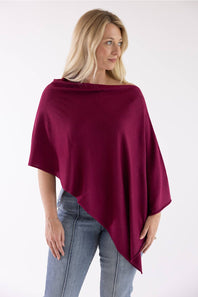 A woman wearing a draped, deep burgundy poncho-style top and light blue jeans, photographed against a plain white studio background.