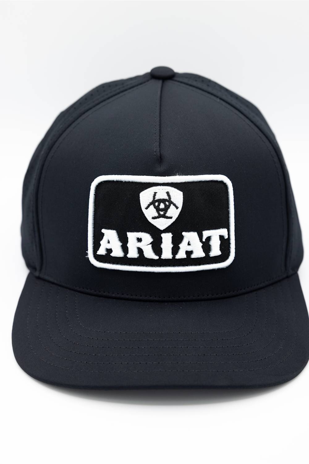 A black baseball cap featuring a white embroidered patch on the front with Ariat's logo and the word 'ARIAT'.