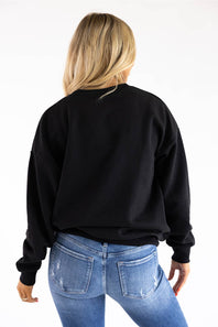 A woman viewed from behind wearing a black crewneck sweatshirt and blue jeans against a plain white background.