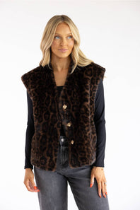 A woman modeling a brown leopard-print faux fur vest over a black long-sleeve top and gray jeans, photographed against a plain white studio background.