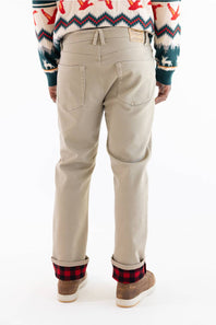 Back view of a person wearing beige chino pants with a red and black buffalo plaid cuff, paired with a patterned sweater and brown shoes, on a white background.