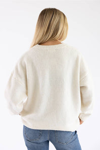 A woman viewed from behind wearing an oversized cream-colored knit sweater and blue jeans against a plain white background.