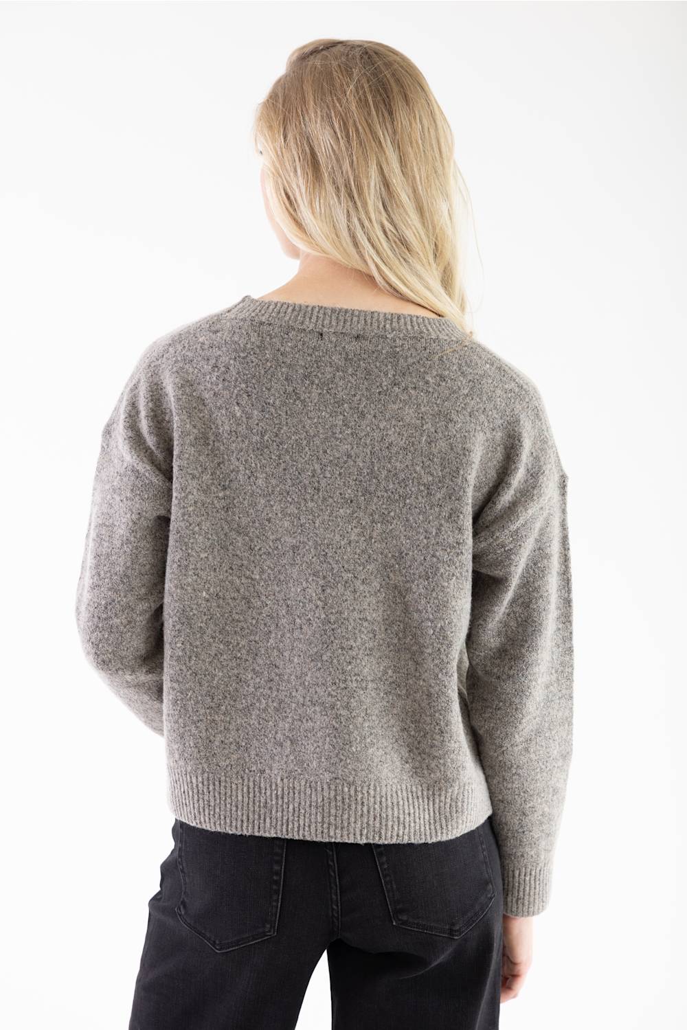 A woman viewed from behind wearing a heathered gray knit sweater and black pants against a plain white background.
